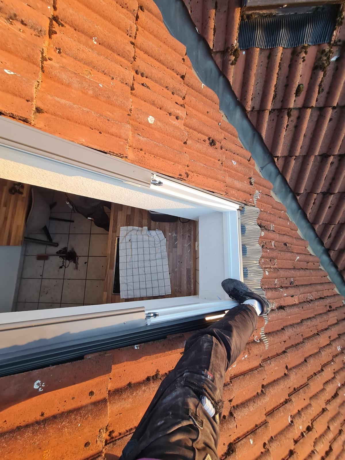 Blick vom Ziegeldach auf den Rahmen eines Dachfensters während des Einbaus
