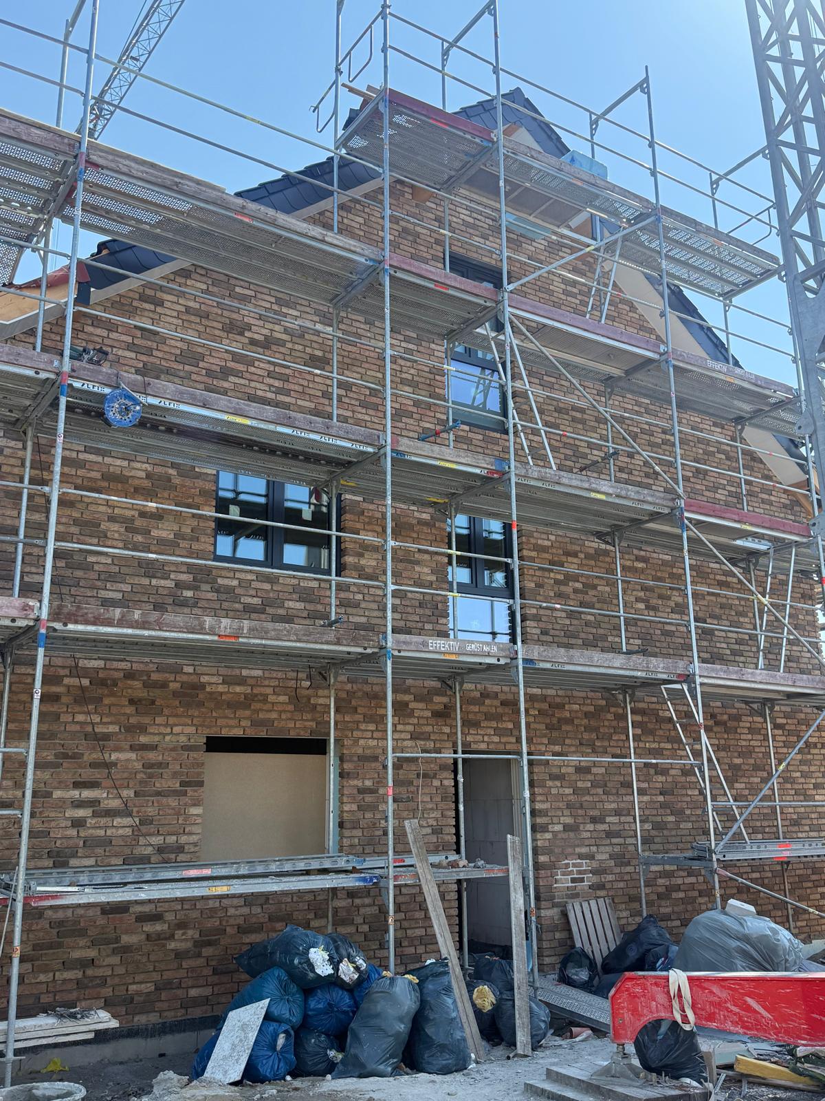 Eingerüsteter Klinkerneubau mit neuen dunklen Fenstern, davor Bauschuttsäcke