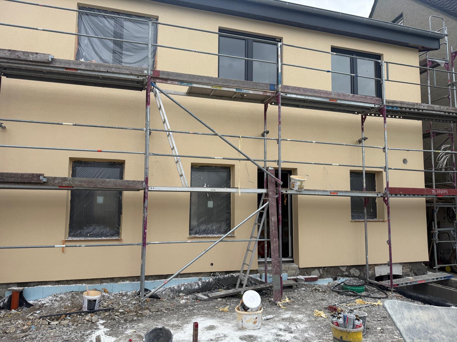 Gelb verputzte Fassade mit neuen Fenstern, teils noch mit Schutzfolie, hinter einem Gerüst