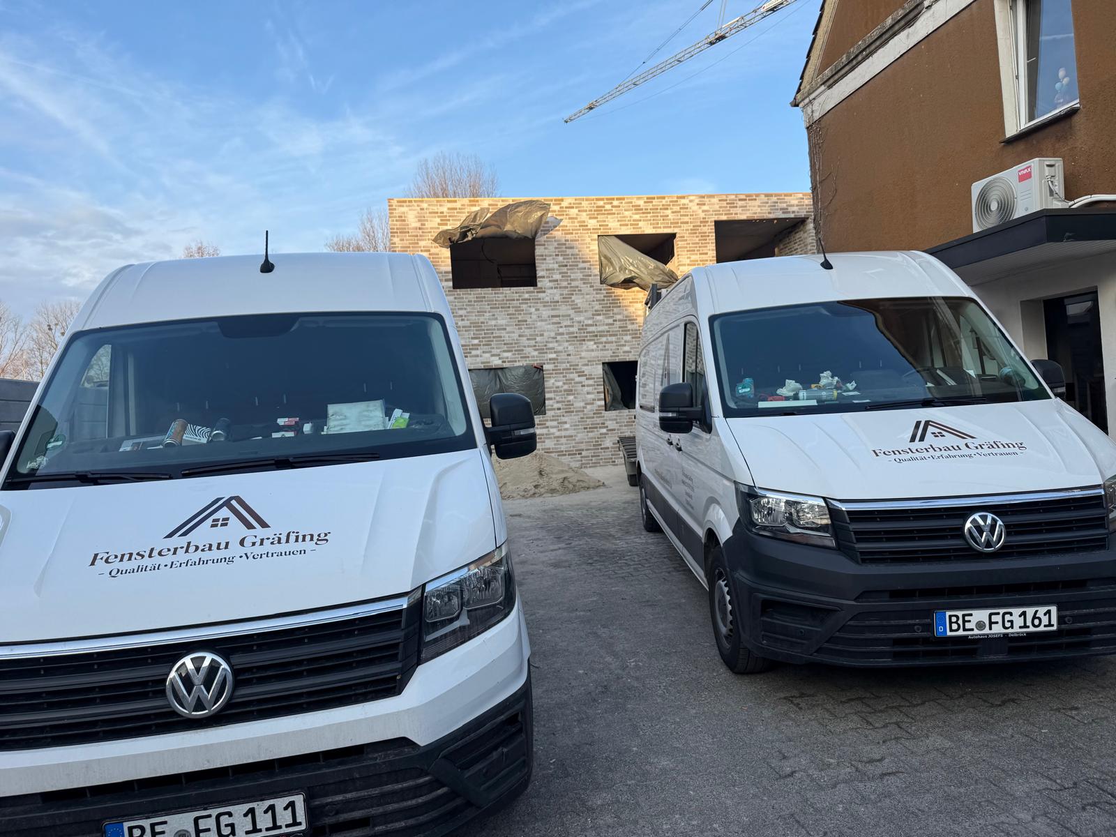 Zwei weiße Transporter von Fensterbau Gräfing vor einem Klinkerrohbau