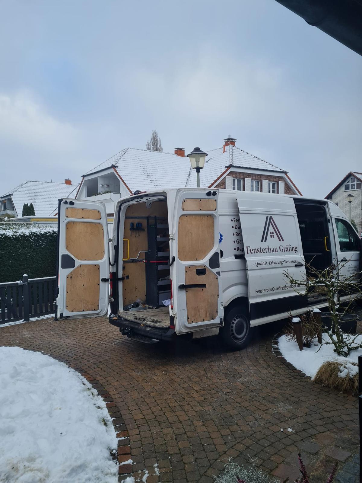 Firmenwagen mit geöffneten Hecktüren auf einer Einfahrt mit Schneeresten