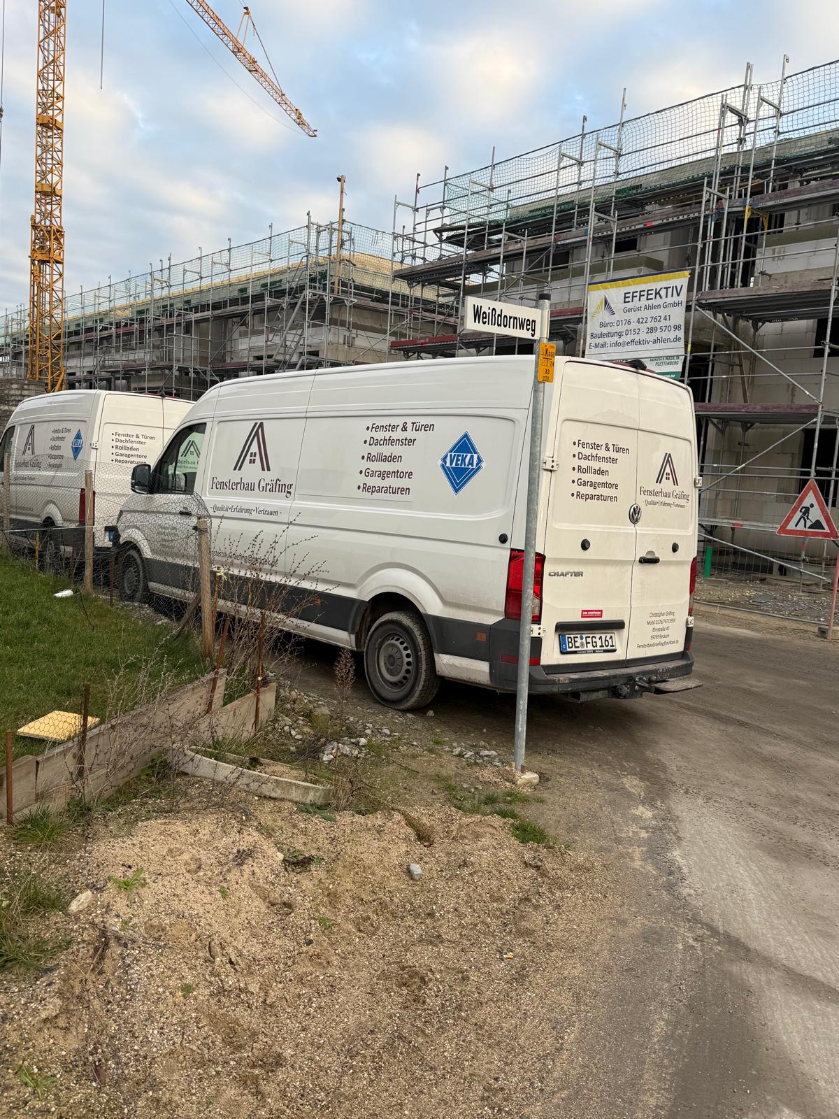 Zwei Firmenwagen von Fensterbau Gräfing vor eingerüsteten Neubauten mit Baukran