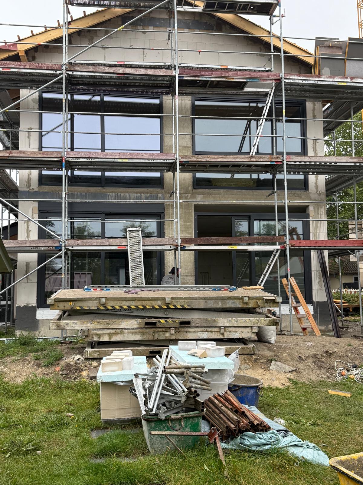 Eingerüsteter Rohbau mit großen dunklen Fensterelementen auf drei Etagen