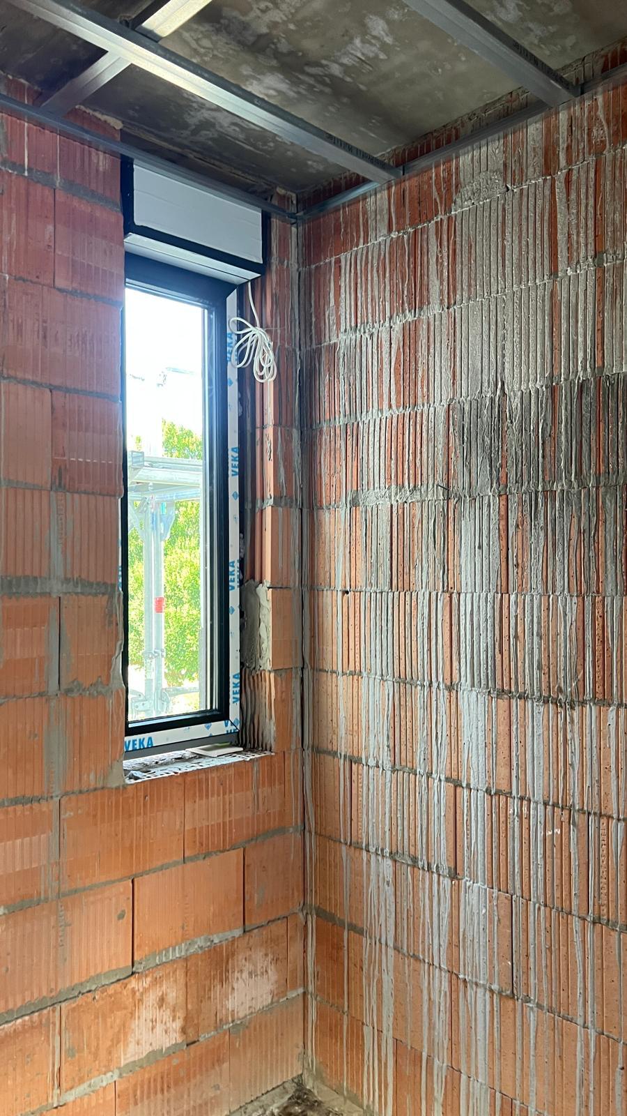 Schmales, hohes Fenster in der Ecke eines unverputzten Ziegelraums