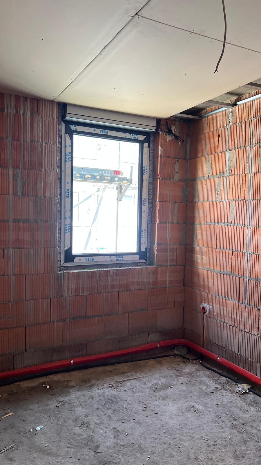 Unverputzter Ziegelraum mit neu eingebautem Fenster und Rollladenkasten