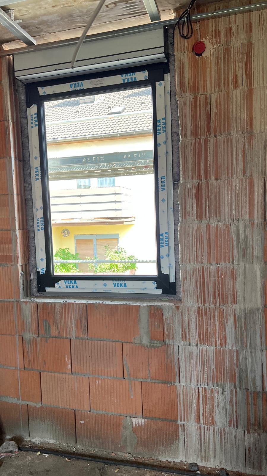 Neu eingebautes Fenster mit Schutzfolie in einer Ziegelwand, dahinter ein Nachbarhaus