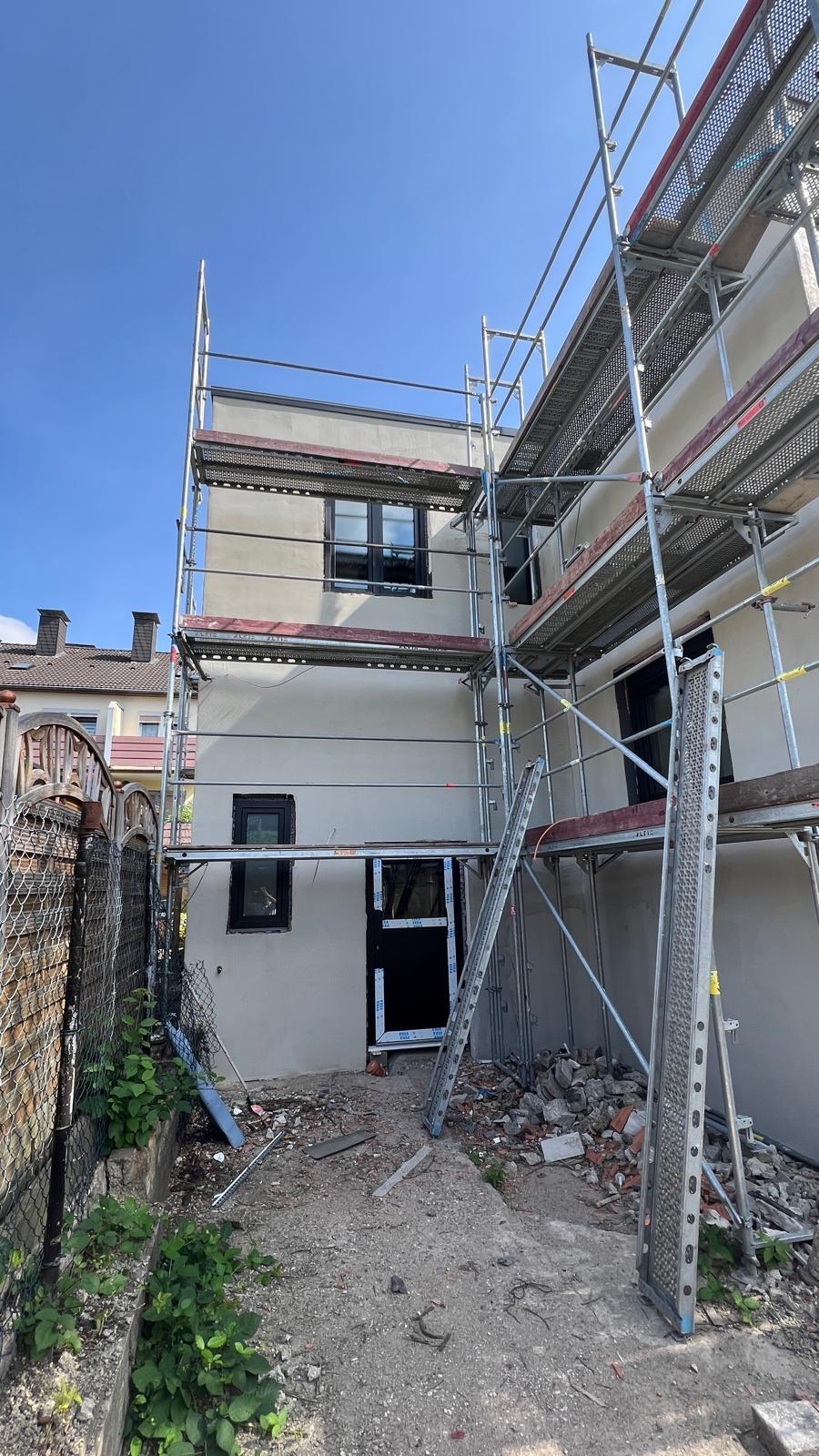 Schmaler Hof mit Gerüst an einem verputzten Haus mit neuen Fenstern