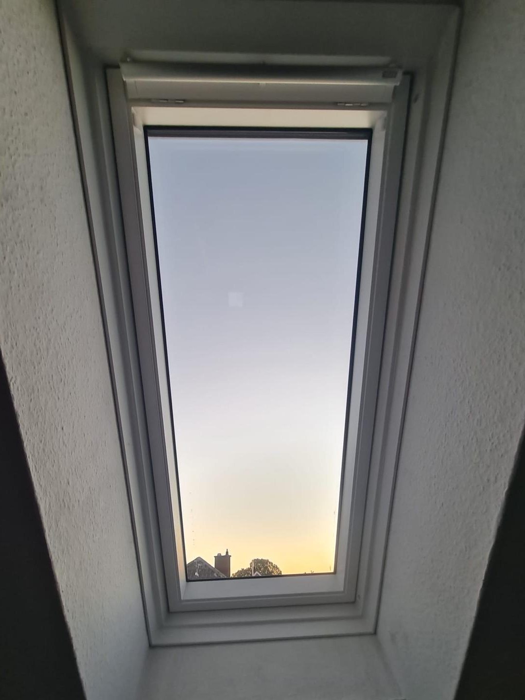 Blick von innen nach oben durch ein Dachfenster in den Abendhimmel