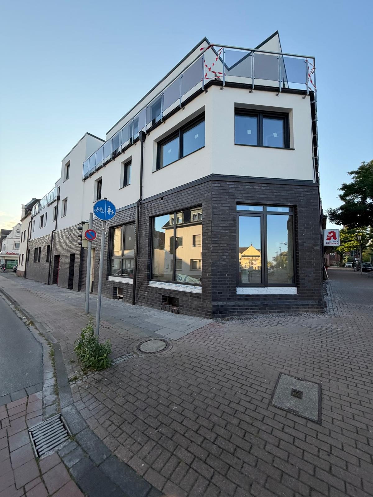 Mehrgeschossiges Eckgebäude mit dunklem Klinkersockel, weißer Putzfassade und großen dunkel gerahmten Fenstern