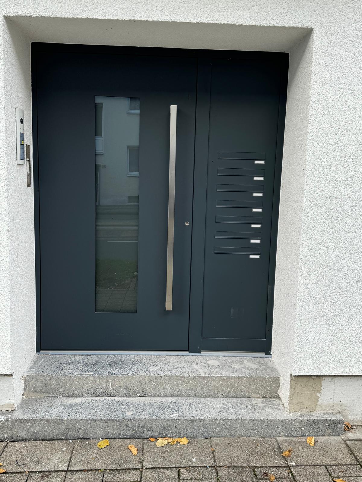 Anthrazitfarbene Haustür mit Glasstreifen, Stangengriff und Briefkästen im Seitenteil