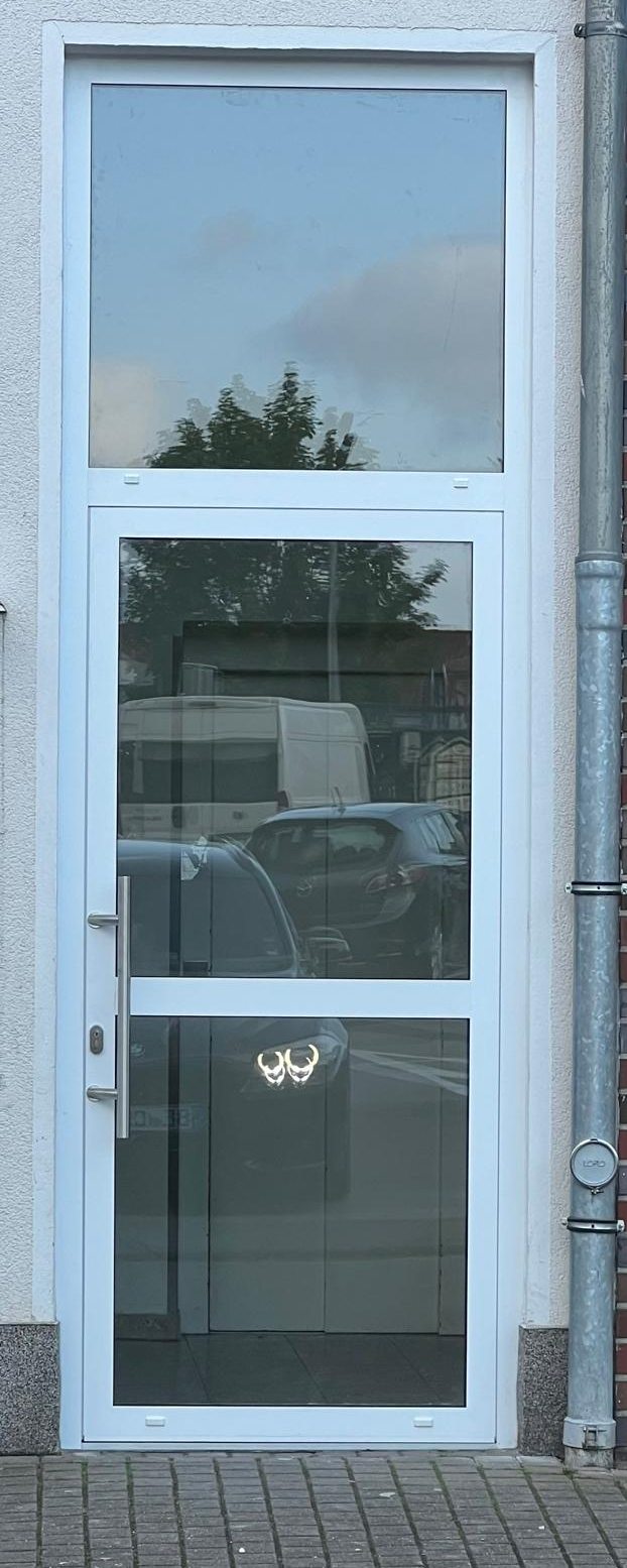 Hohe weiße Glastür mit Oberlicht in einer hellen Fassade