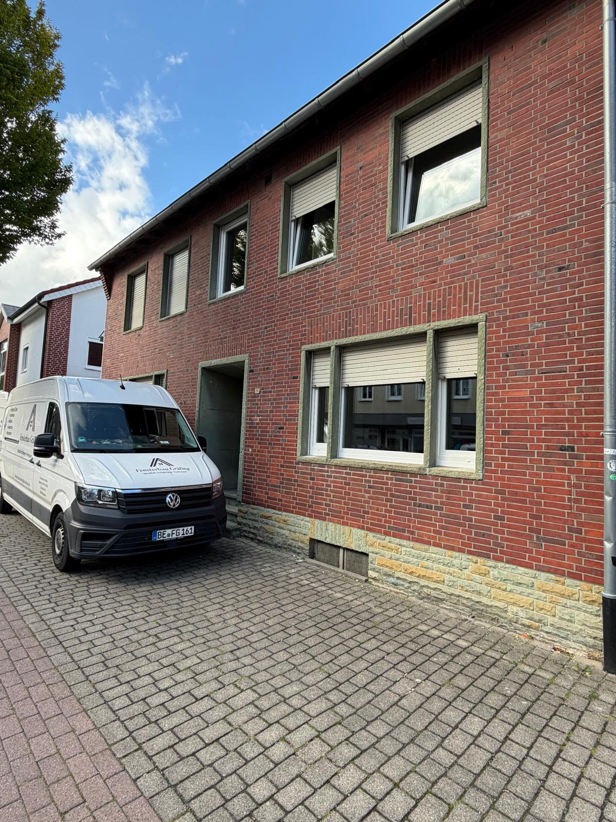 Rotes Klinkerhaus mit hell eingefassten Fenstern und teils geschlossenen Rollläden, davor der Firmenwagen