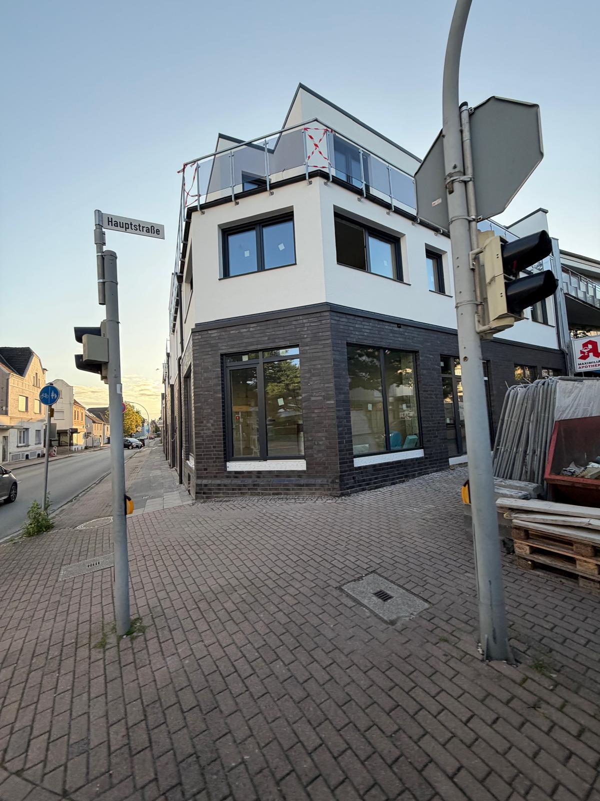Eckgebäude mit großen dunkel gerahmten Fenstern an einer Straßenkreuzung im Abendlicht