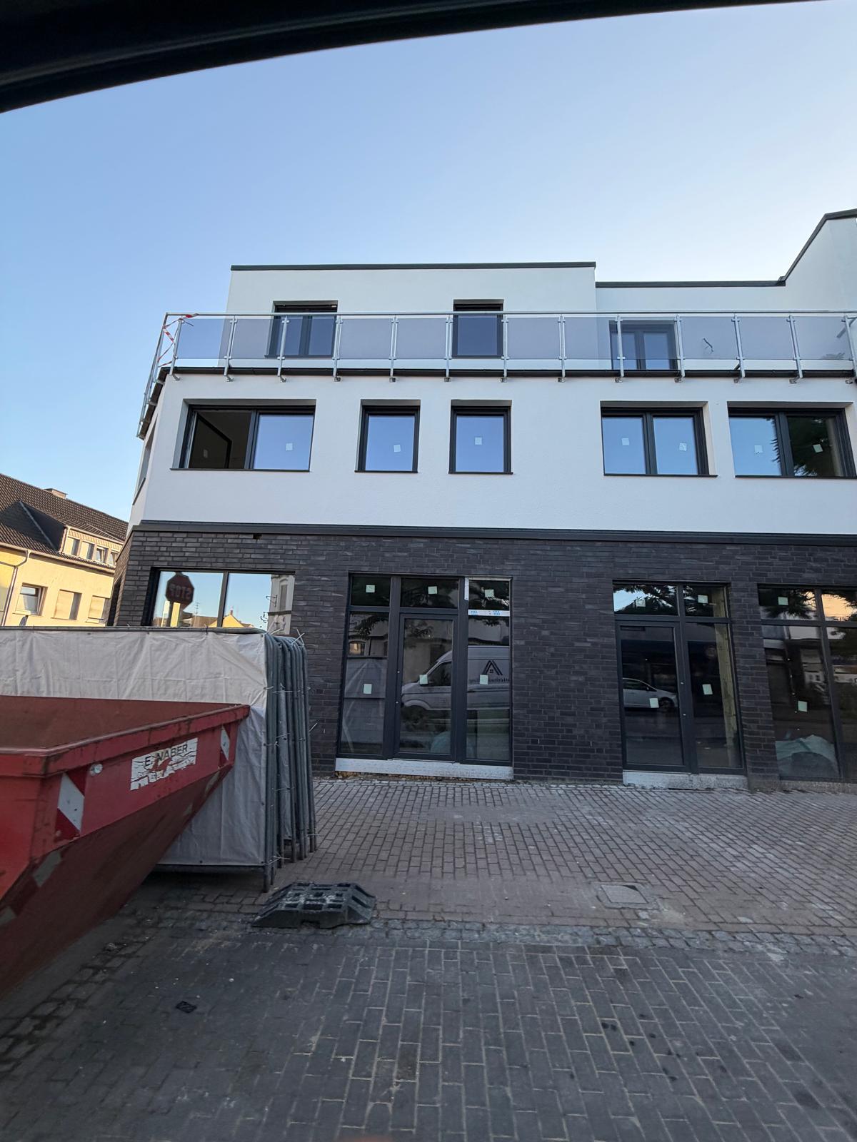Gebäude mit dunklem Klinker im Erdgeschoss, bodentiefen Fenstern und weißer Fassade mit Glasgeländer darüber