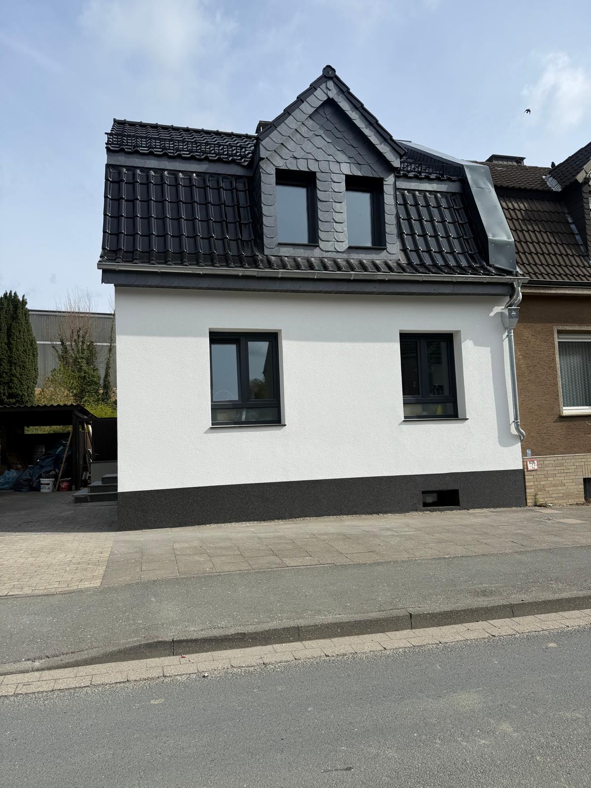 Kleines weißes Wohnhaus mit dunklem Dach, Schiefergaube und anthrazitfarbenen Fenstern