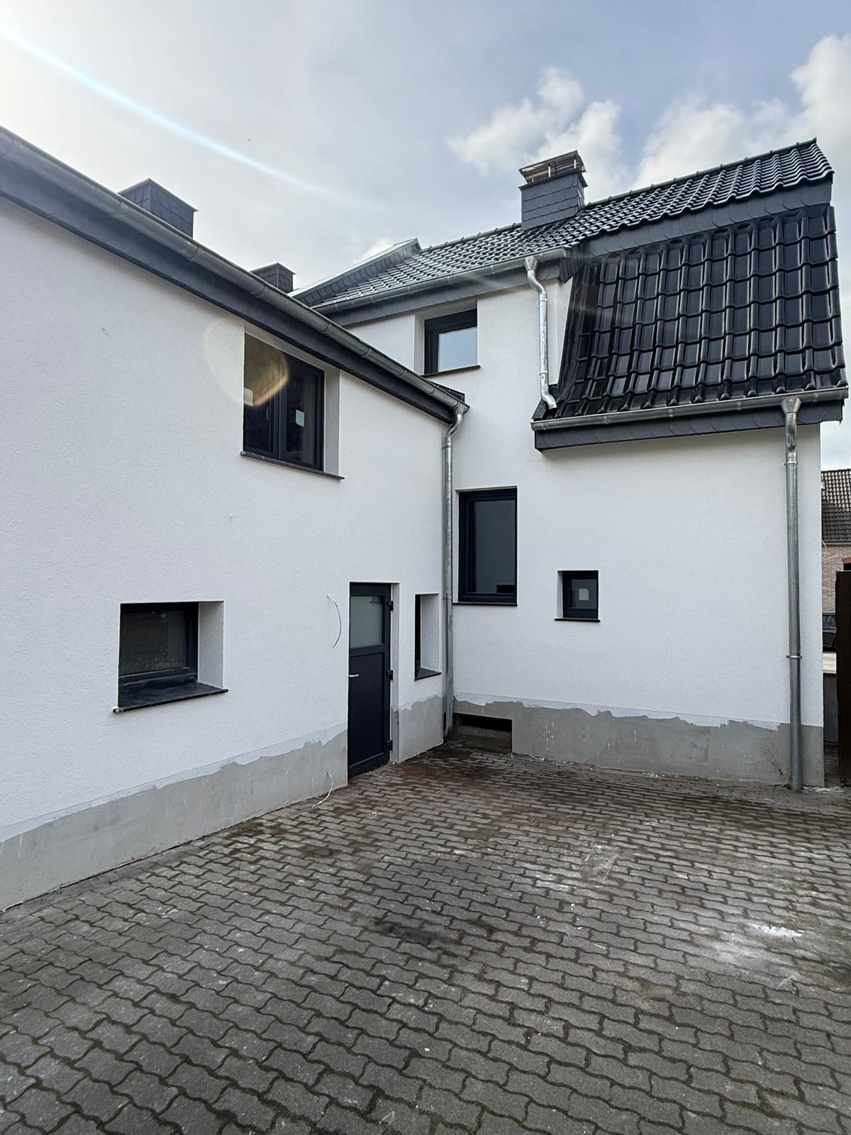 Innenhof zwischen weißen Hausfassaden mit anthrazitfarbenen Fenstern und einer Nebentür
