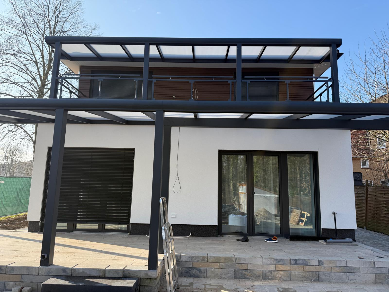 Weißes Haus mit überdachter Terrasse, bodentiefen Fenstertüren und geschlossener Außenjalousie