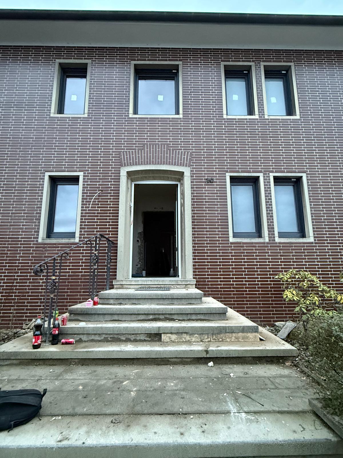 Dunkle Klinkerfassade eines Mehrfamilienhauses mit hell eingefassten Fenstern und einer Eingangstreppe