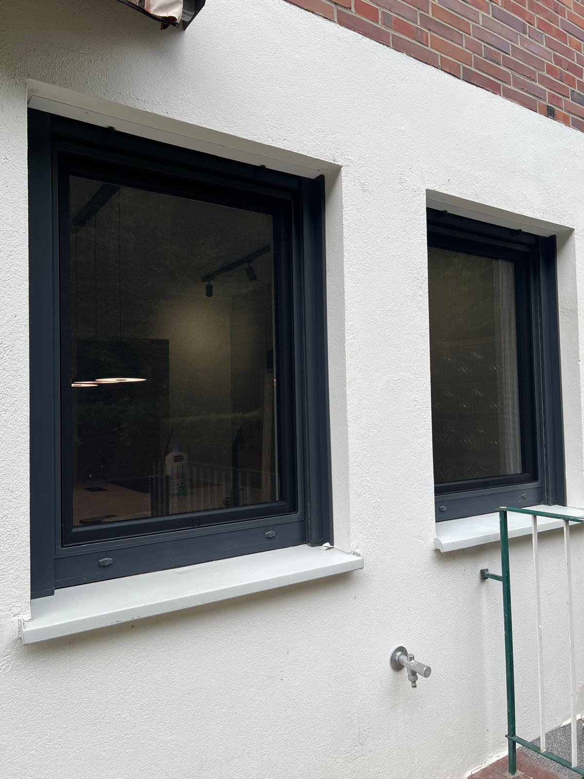Zwei anthrazitfarbene Fenster mit hellen Fensterbänken in einer cremefarbenen Putzfassade