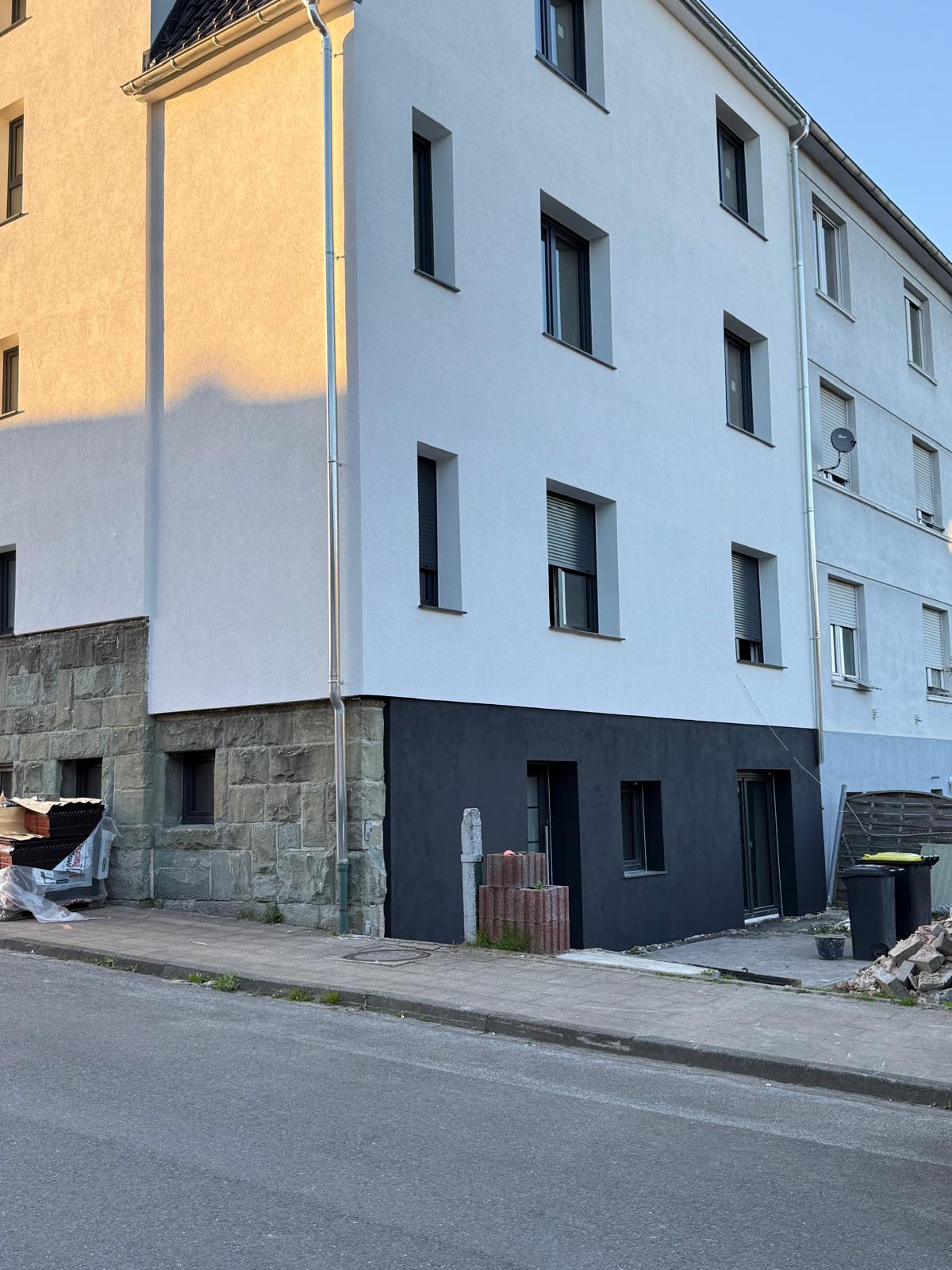 Mehrgeschossiges weißes Eckhaus mit dunklem Sockel und schmalen, dunkel gerahmten Fenstern