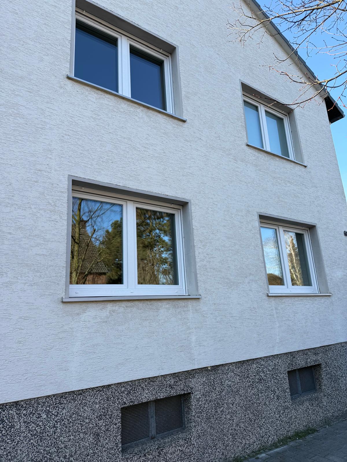 Helle Putzfassade mit vier weißen, zweiflügeligen Fenstern