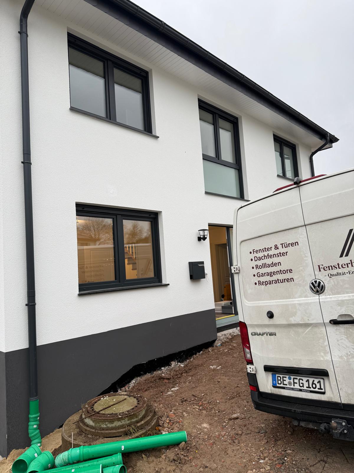 Weißer Neubau mit dunklem Sockel und anthrazitfarbenen Fenstern, daneben das Heck des Firmenwagens
