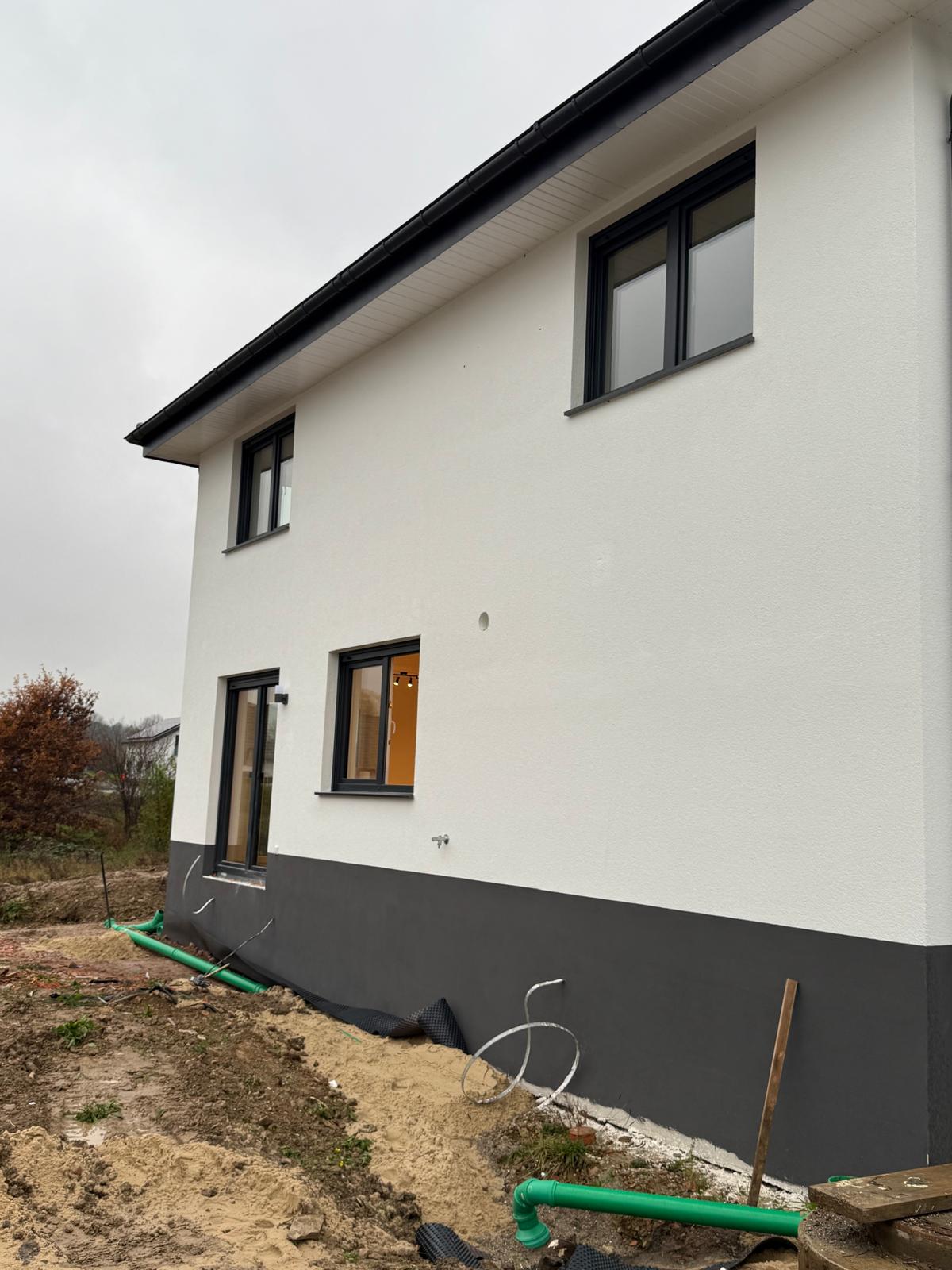 Weißer Neubau mit dunklem Sockel, anthrazitfarbenen Fenstern und einer Terrassentür