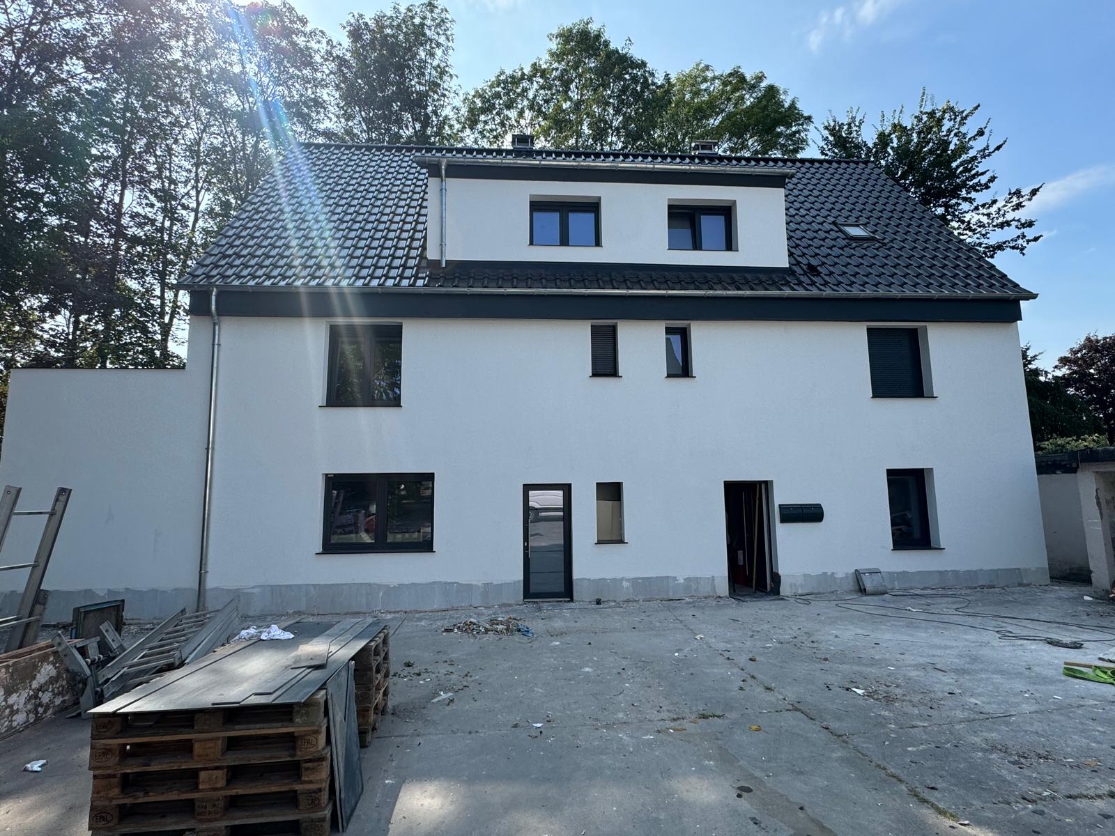 Weißes Mehrfamilienhaus mit dunklem Dach, Gaube und dunkel gerahmten Fenstern an einem gepflasterten Hof