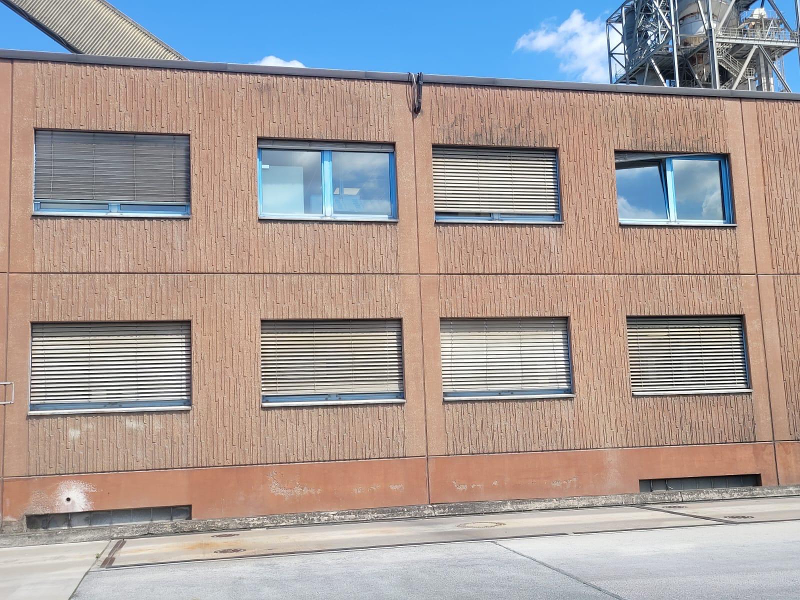 Rotbraune Gewerbefassade mit acht Fenstern, die meisten mit geschlossenen hellen Jalousien