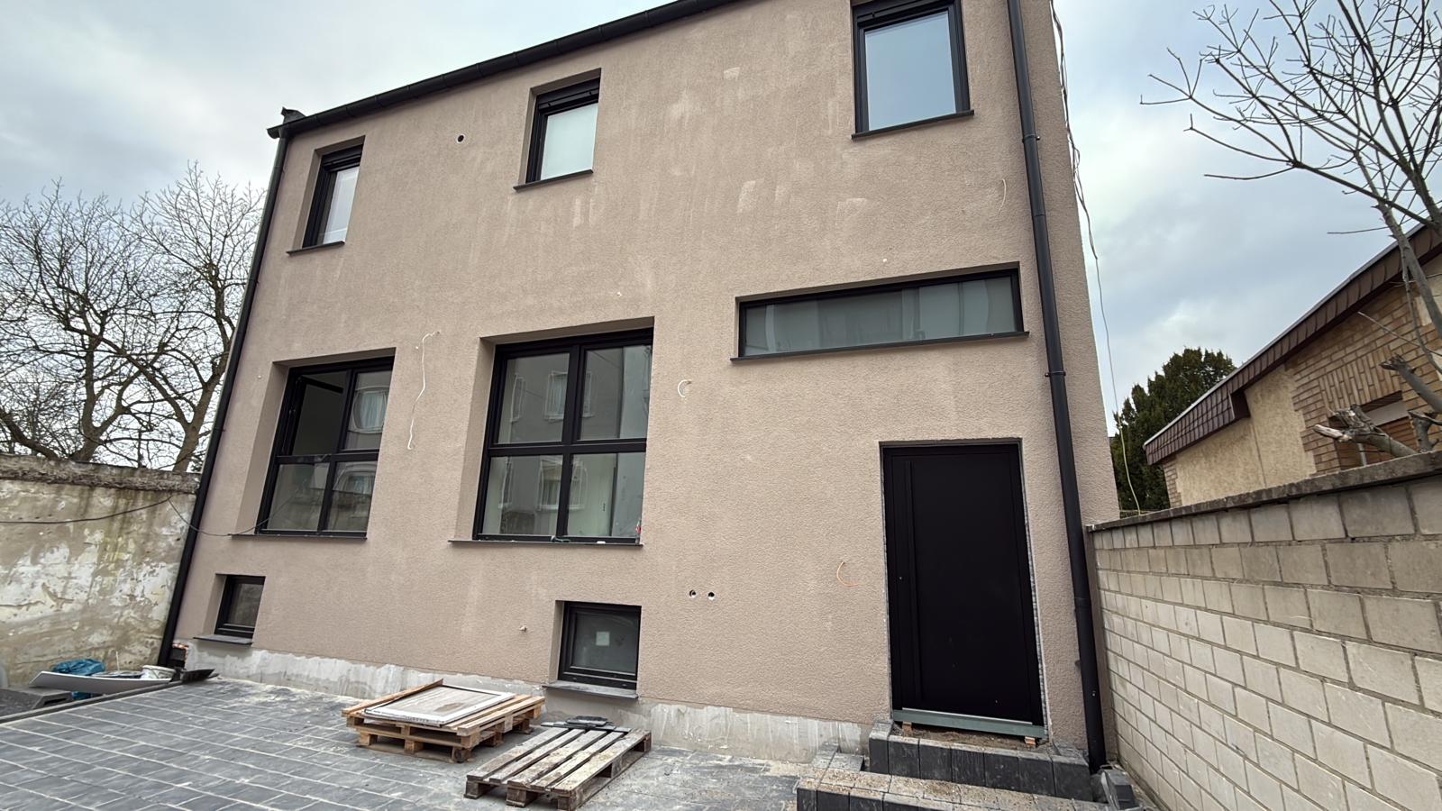 Verputztes Haus mit dunkel gerahmten Fenstern und dunkler Nebentür an einem gepflasterten Hof