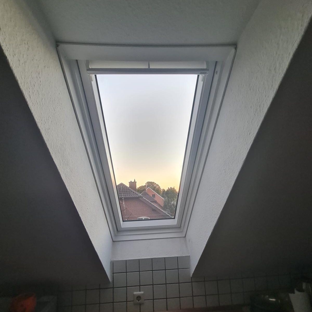 Blick aus einem dunklen Raum nach oben durch ein Dachfenster in den Abendhimmel
