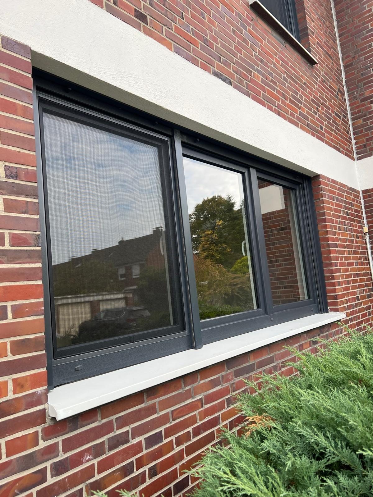 Dreiteiliges anthrazitfarbenes Fenster mit heller Fensterbank in einer roten Klinkerfassade