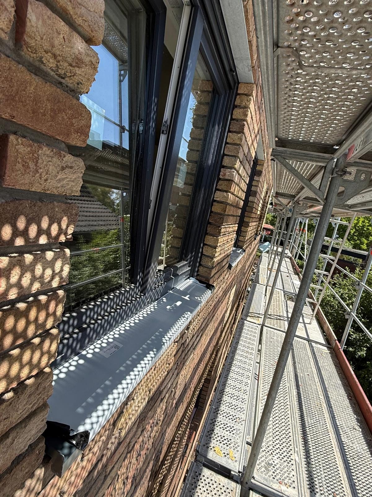 Nahaufnahme eines neu eingebauten Fensters mit Metallfensterbank, vom Baugerüst aus fotografiert