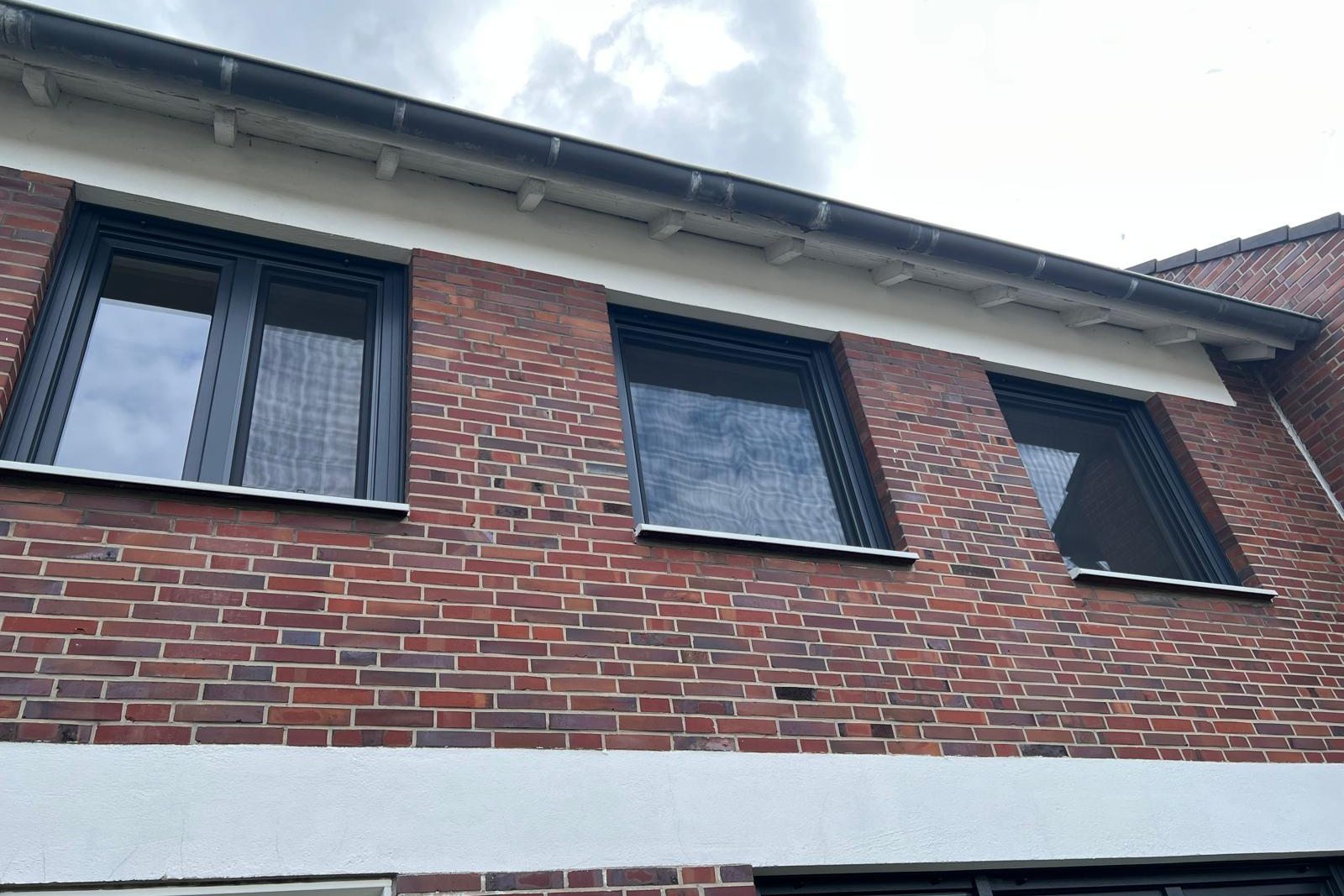 Drei anthrazitfarbene Fenster in einer roten Klinkerfassade, von unten fotografiert