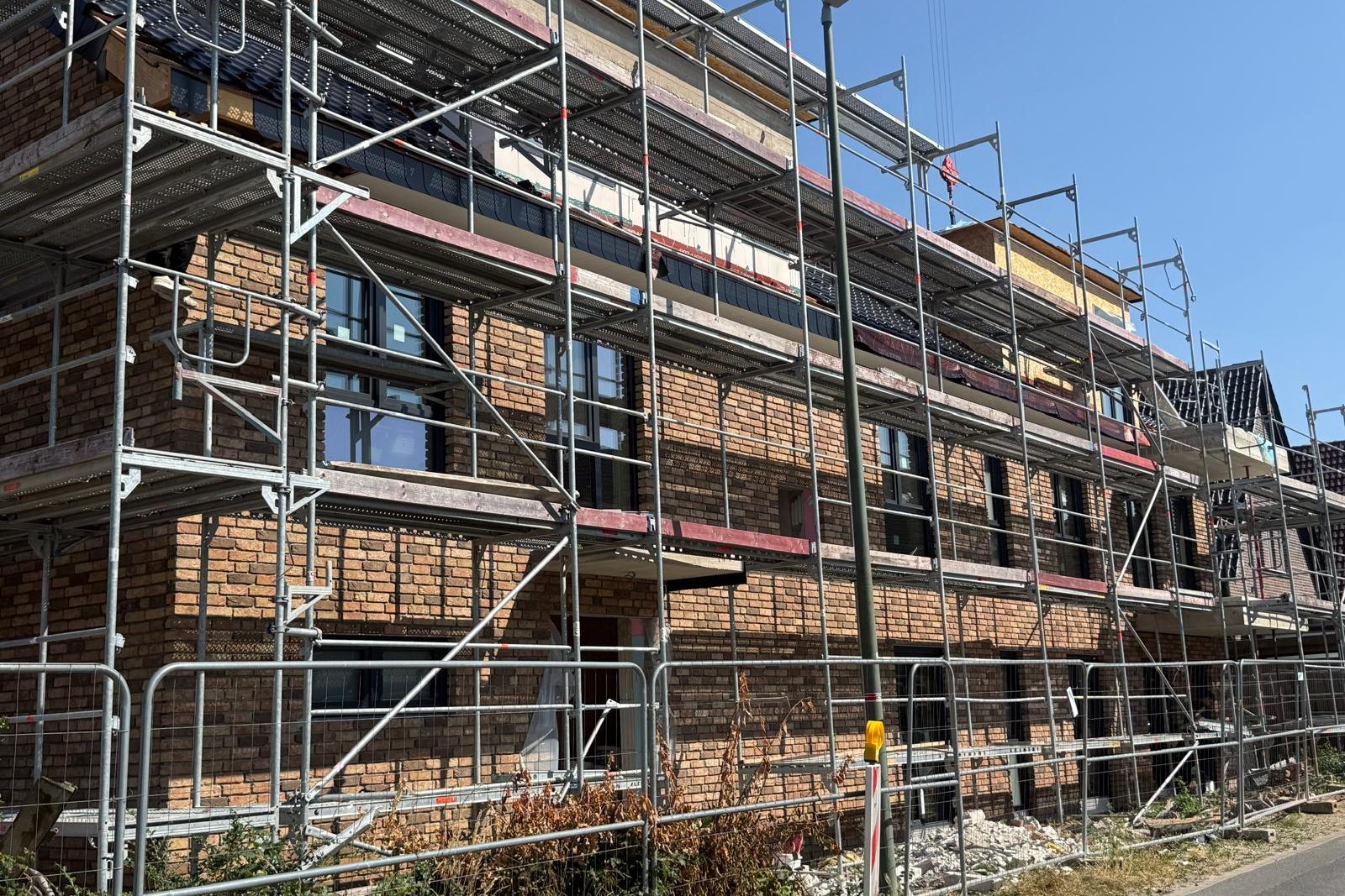 Eingerüstete Klinkerfassade mit neu eingesetzten dunklen Fenstern unter blauem Himmel